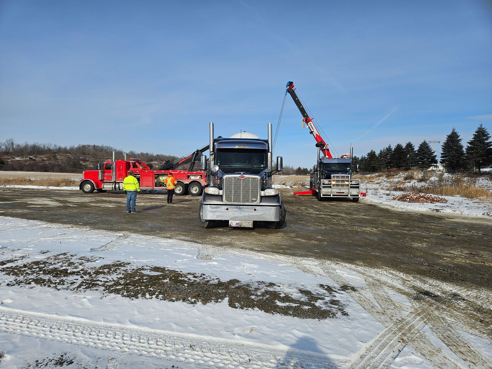 Workers and trucks at a snowy construction site with a crane lifting a load