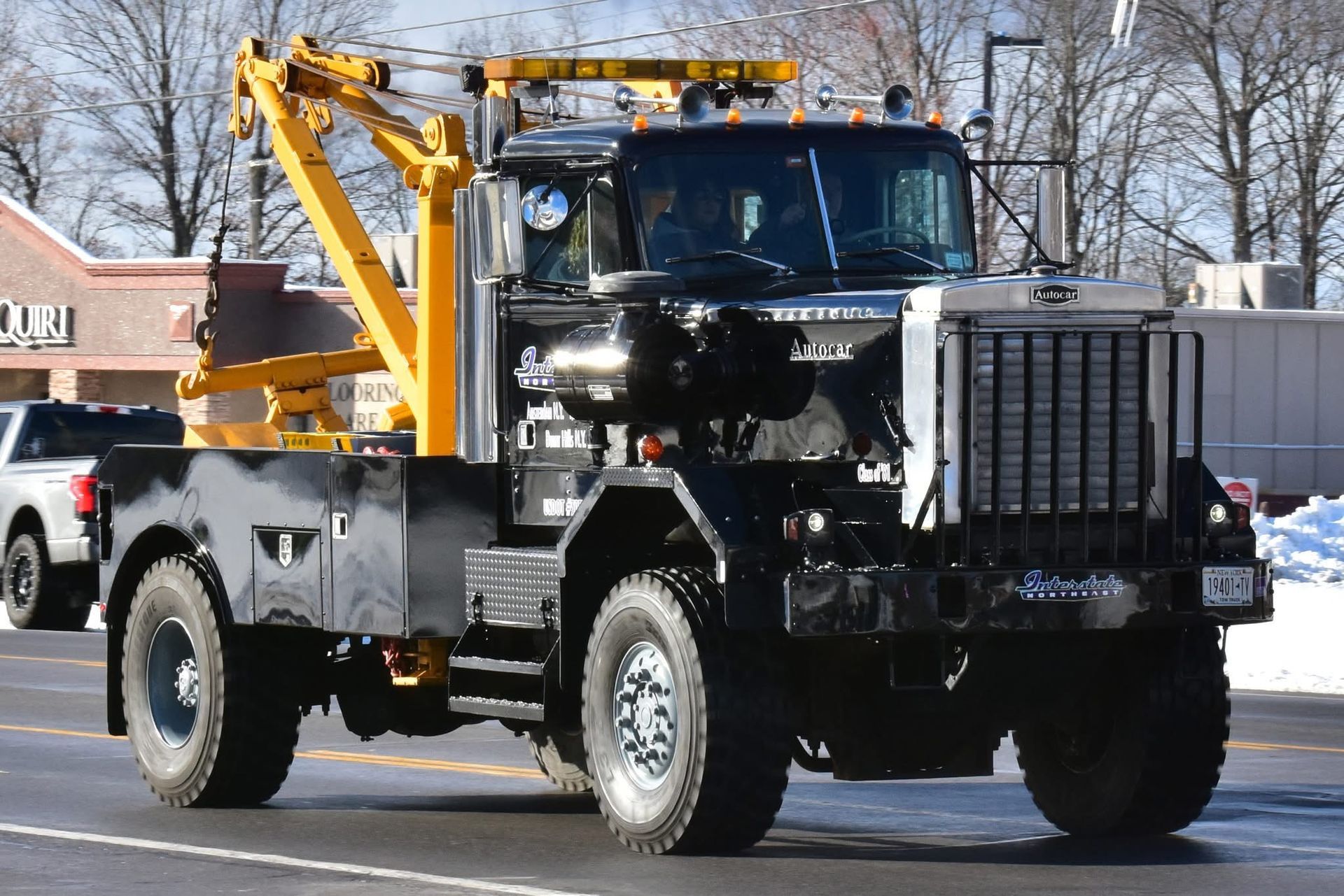 Black tow truck with yellow boom driving on a road, front grille exposed.