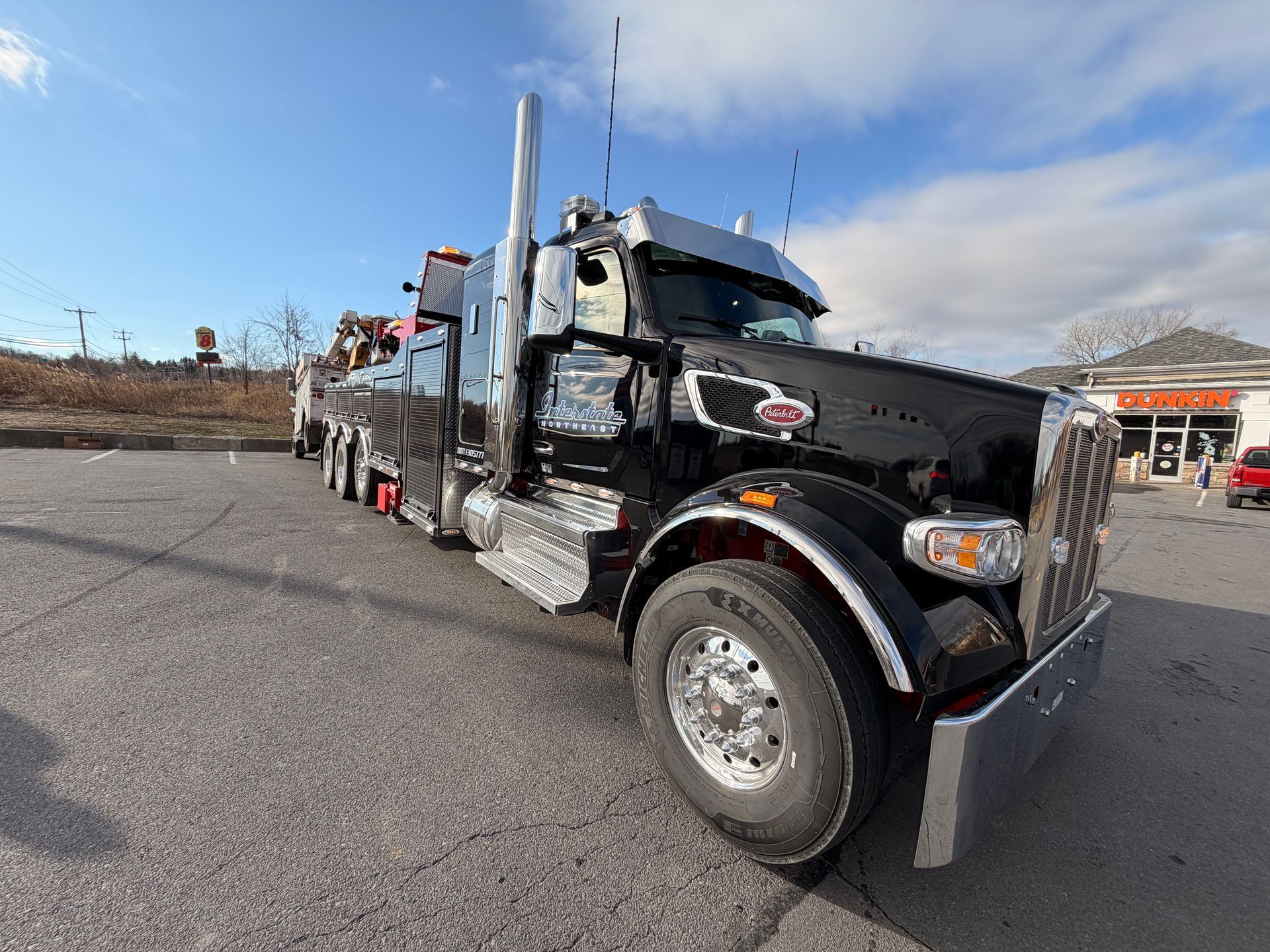 Black semi-truck parked outdoors under a blue sky in a lot