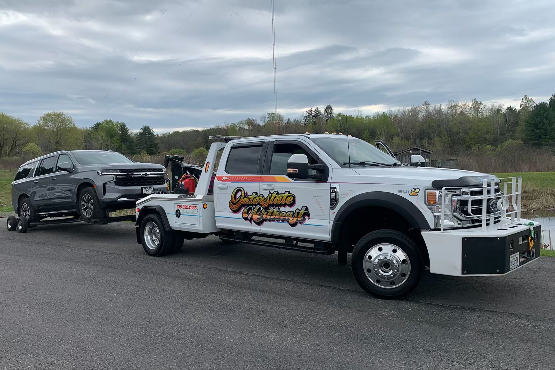 White tow truck hauling a black SUV on a cloudy roadside