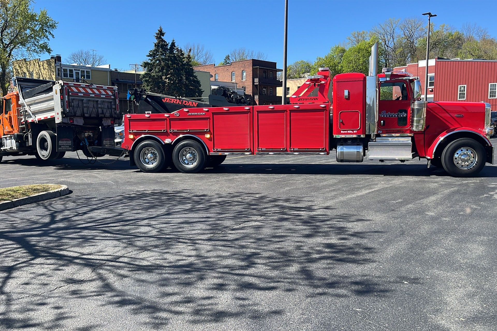 Red semi-truck with flatbed trailer parked in a lot under a clear blue sky