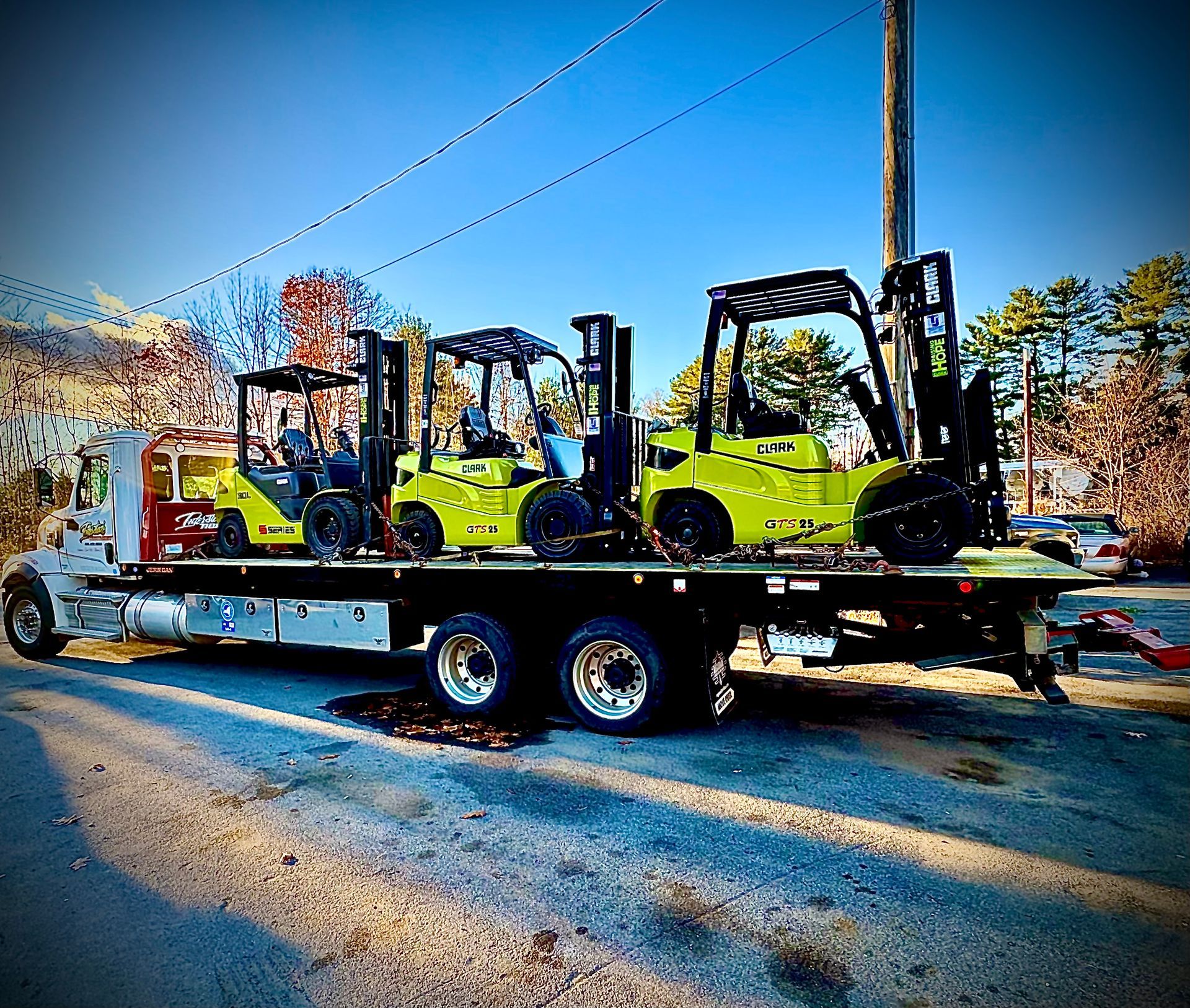 Three lime-green forklifts on a flatbed trailer parked outdoors on a sunny day.