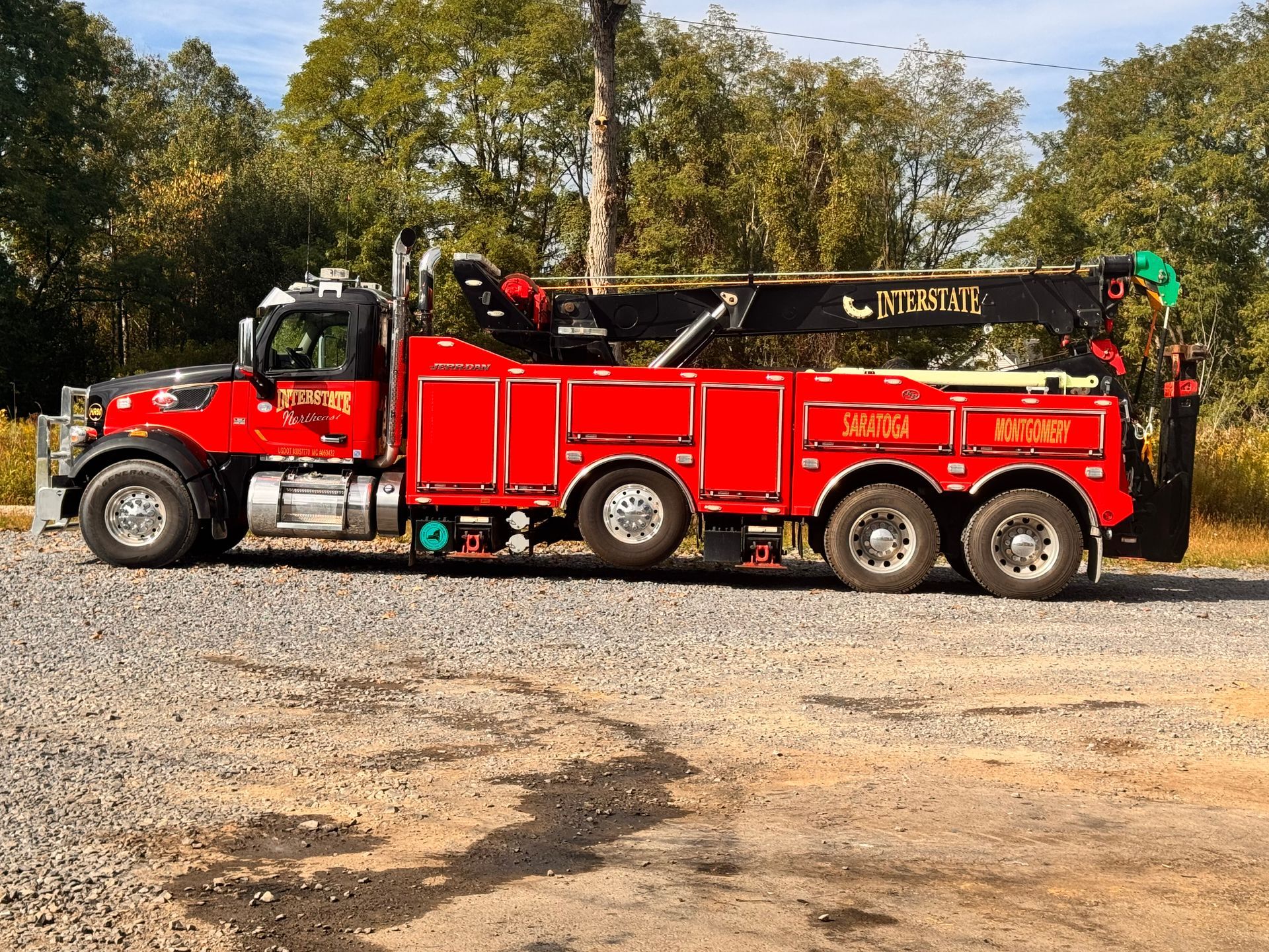 Red fire truck with ladder parked on dirt near trees under a blue sky