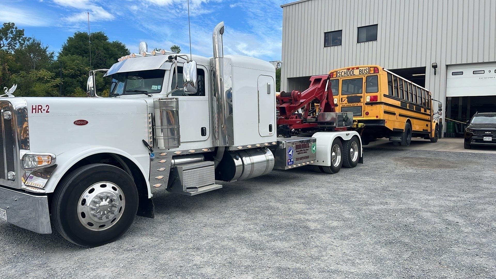 White semi-truck towing a yellow trailer loader in a gravel lot beside a warehouse