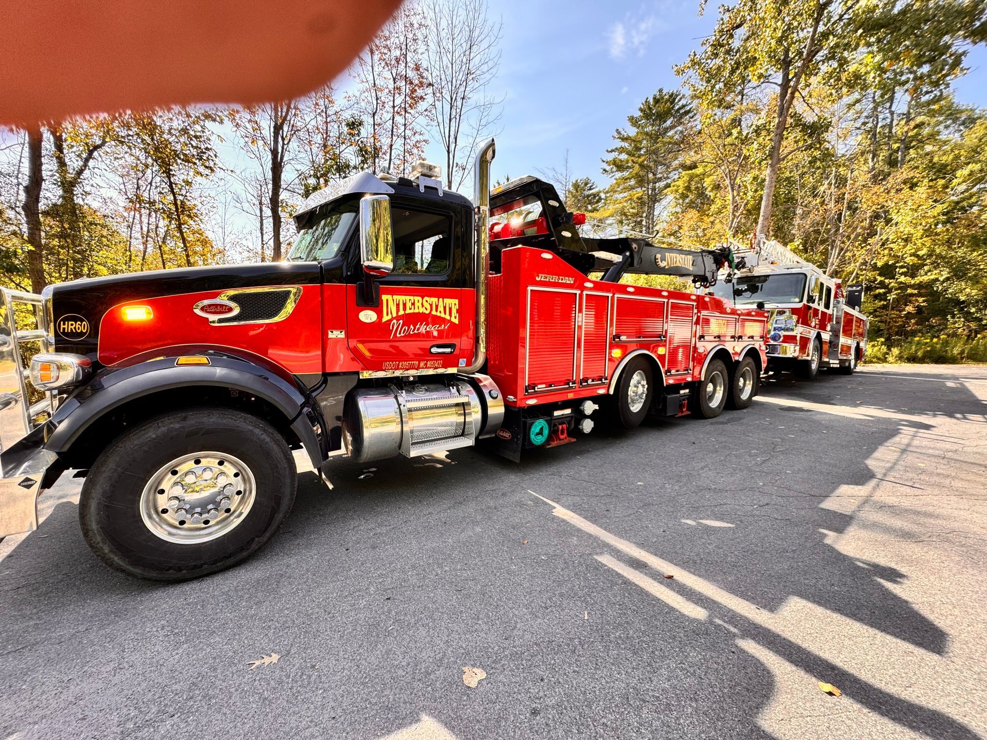 Red heavy-duty tow truck hauling a red tractor trailer on a tree-lined road in daylight