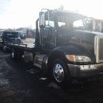 Black semi-truck with flatbed trailer parked outdoors in a lot