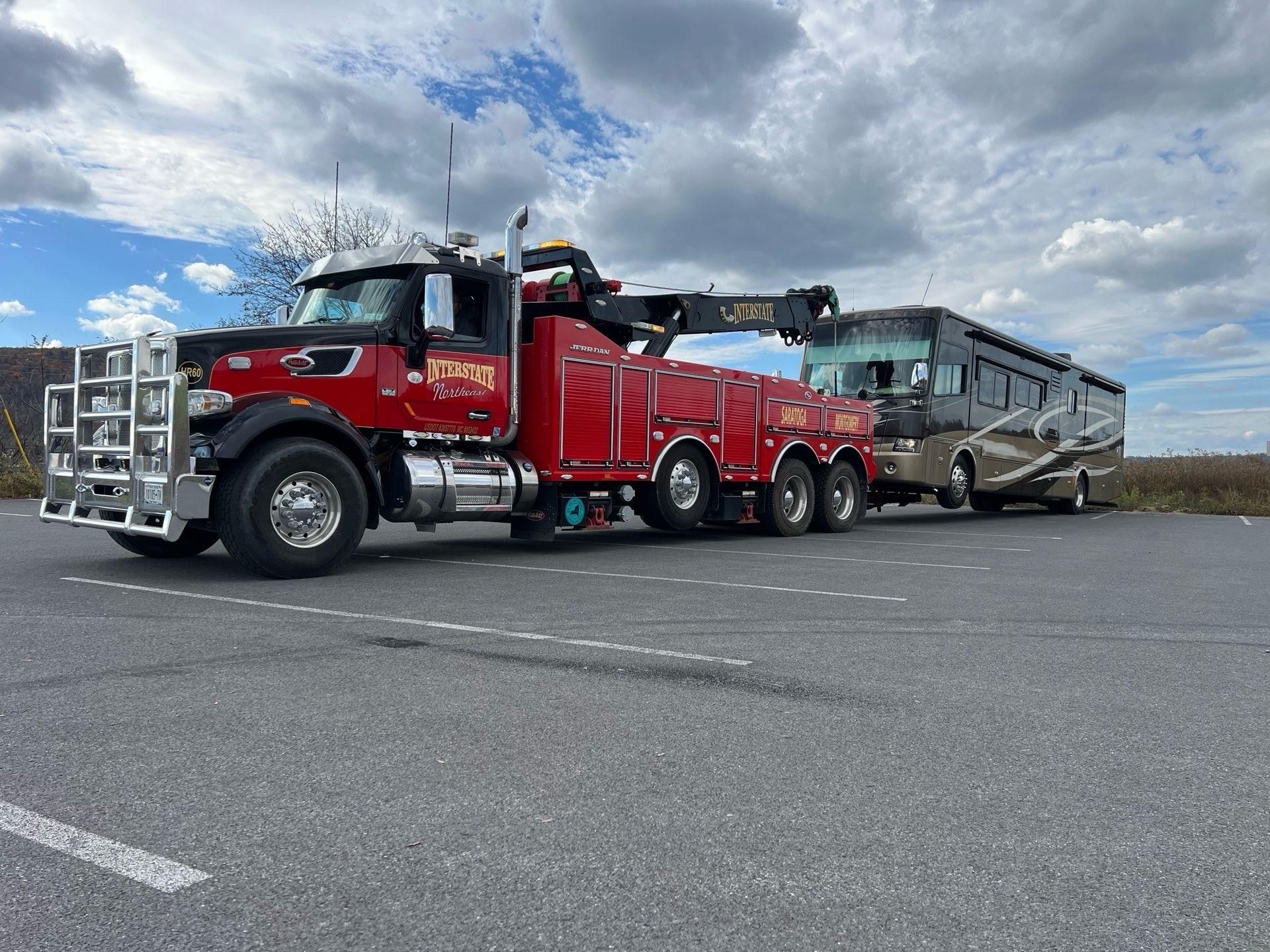 Red tow truck hauling a large damaged bus on a road under a cloudy sky