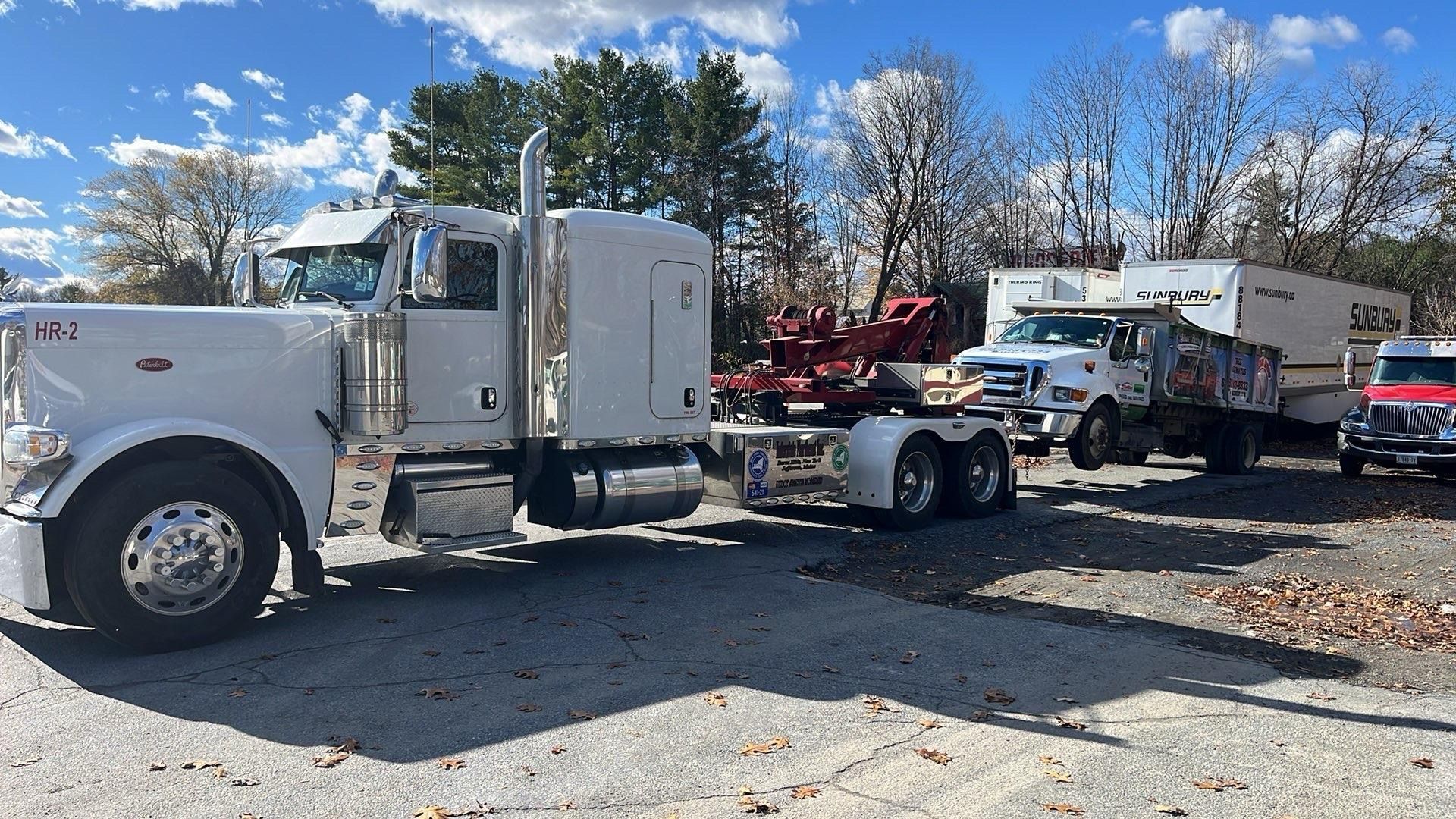 Two white semi trucks parked in a gravel lot on a sunny day