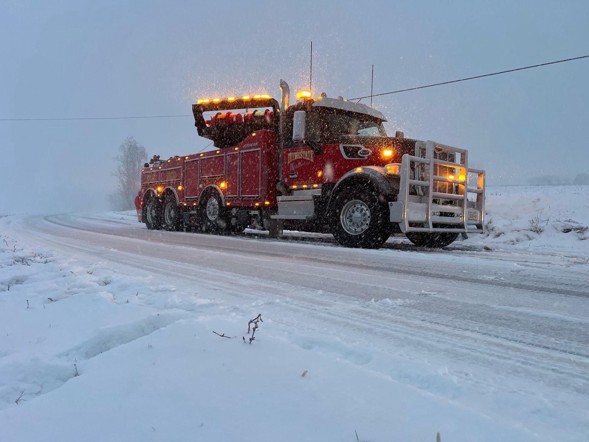 Red tow truck driving on a snowy road in a winter storm