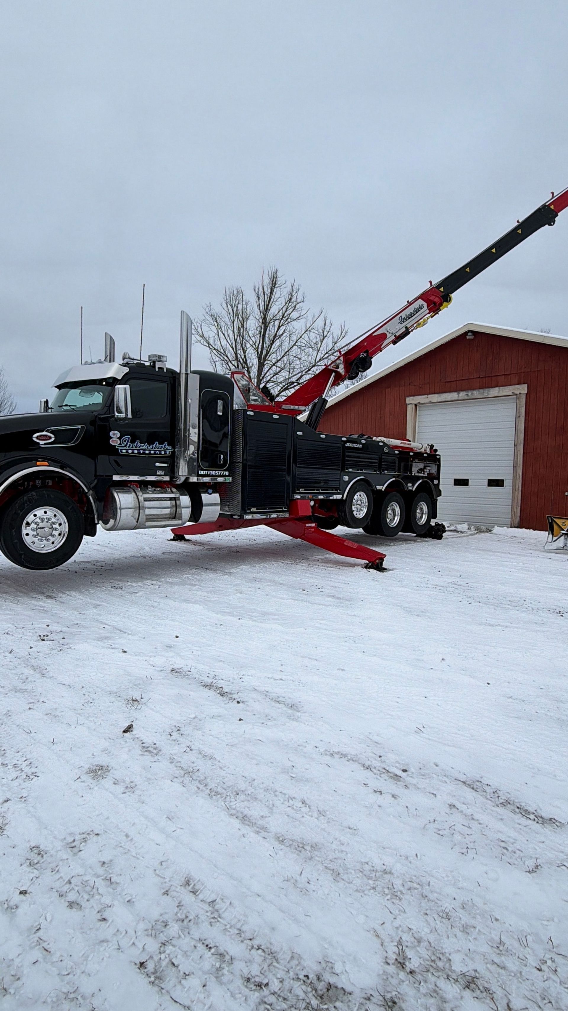 Snowy roadside scene with a black truck and red snowplow in front of a red garage