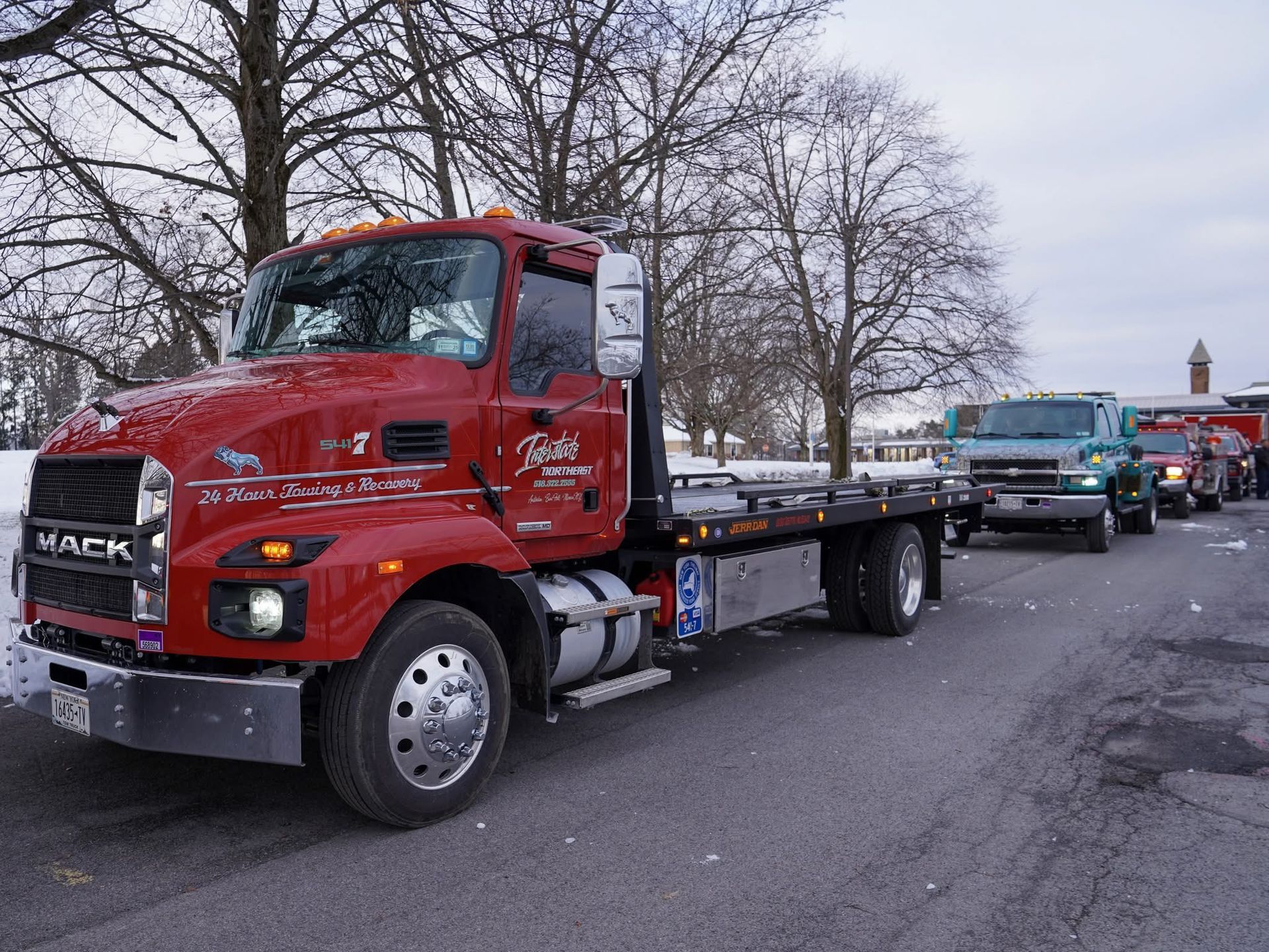 Red Mack flatbed tow truck parked on a street with other trucks lined up behind it.