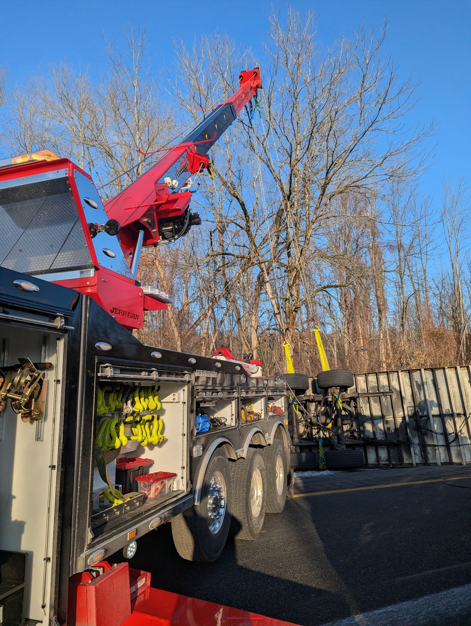Red crane boom mounted on a truck beside a building and trees under a blue sky