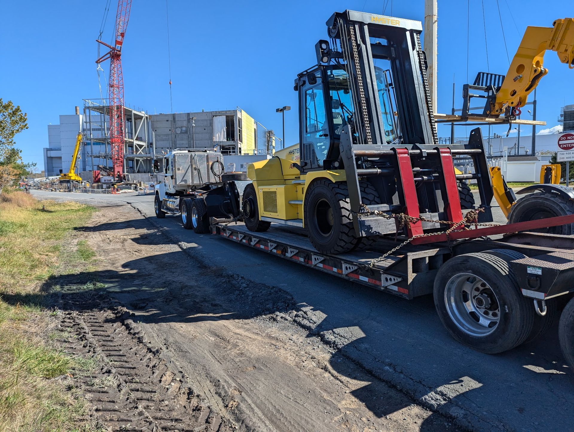 Loaded construction equipment on a flatbed trailer beside a road at a worksite