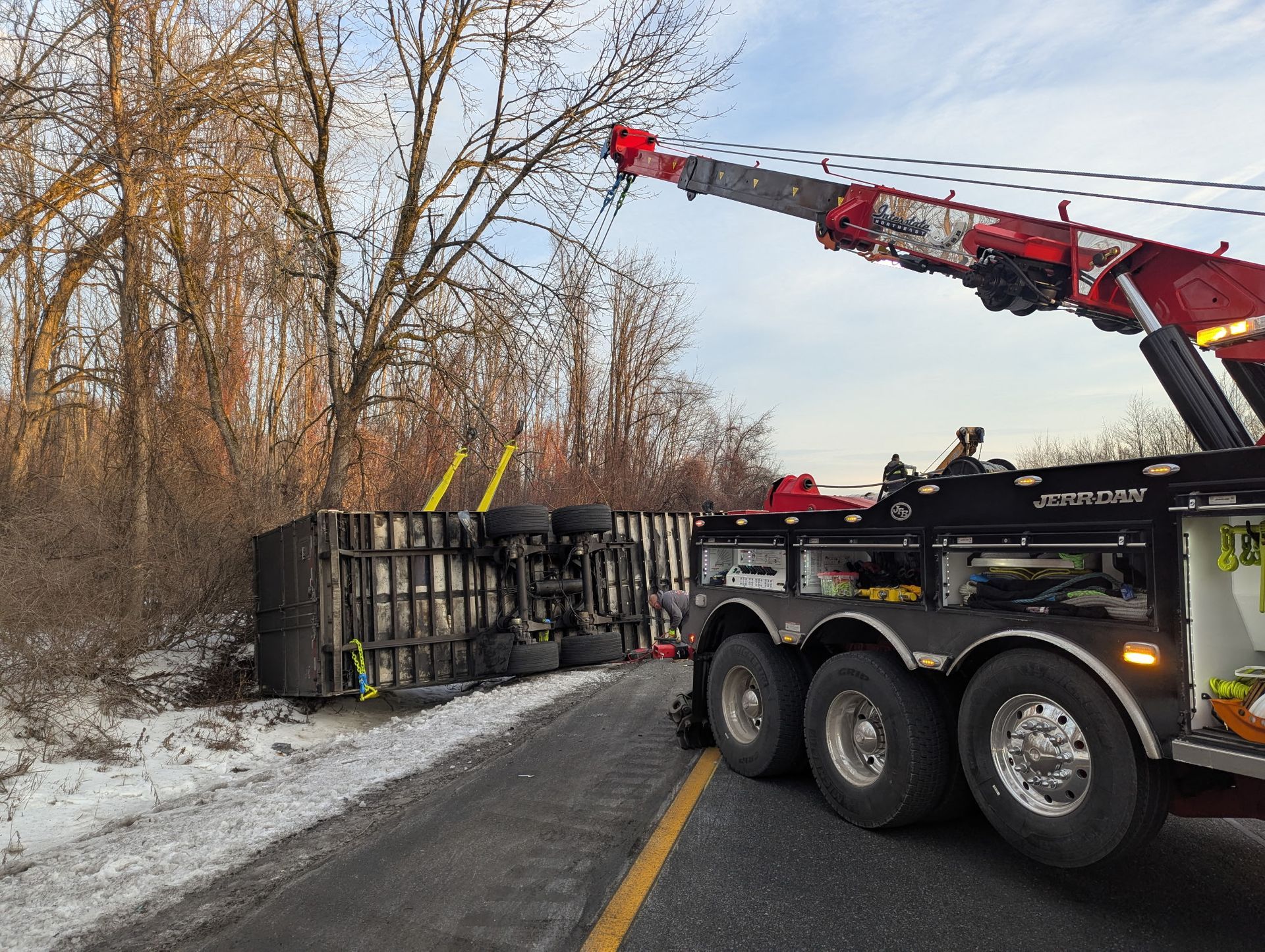 Tow truck with raised crane overturning a trailer on a snowy roadside