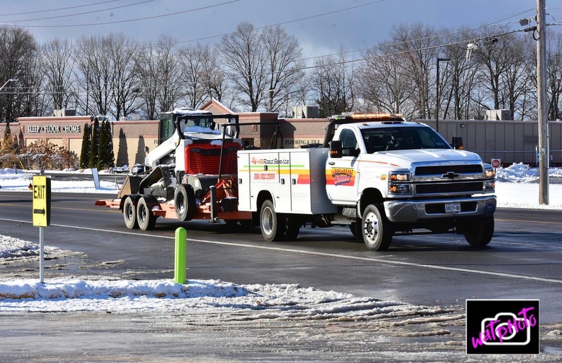 White utility truck towing a red trailer on a snowy road near a parking lot
