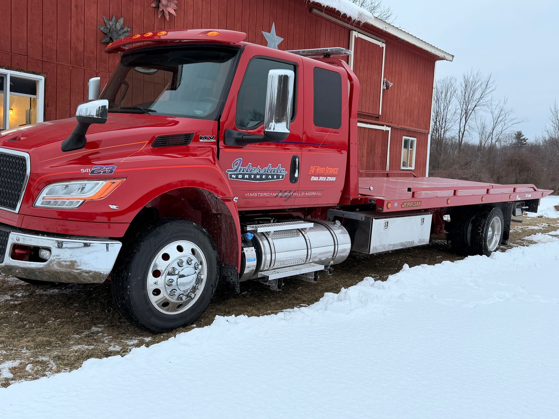 Red flatbed truck parked in snowy yard beside a red barn