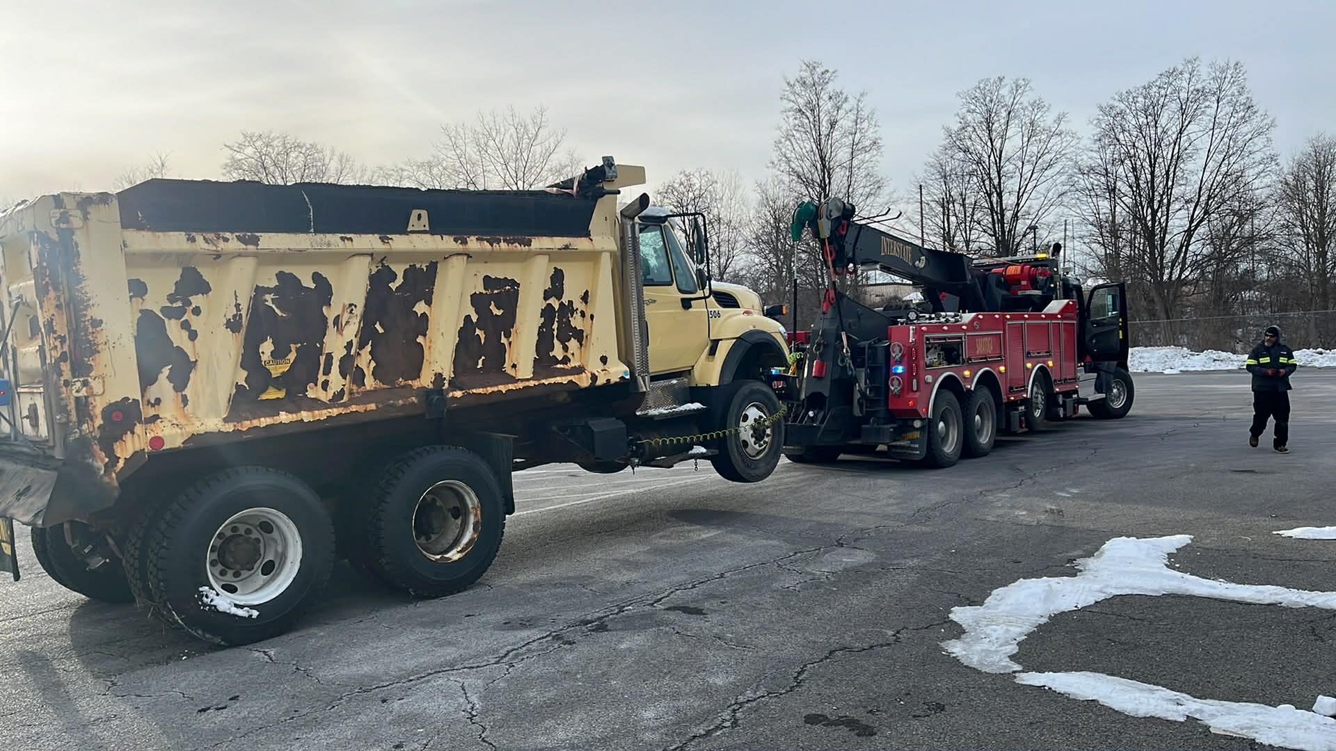 Yellow dump truck being towed by a red heavy-duty wrecker on a snowy road