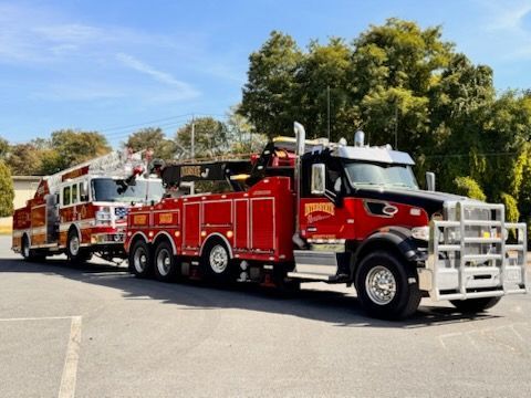 Red fire truck with ladder parked on a sunny street, with trees and blue sky in the background