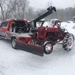Red tow truck clearing a snow-covered vehicle in a snowy lot