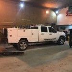 White utility pickup truck parked at night beside a brick building under warm lights.