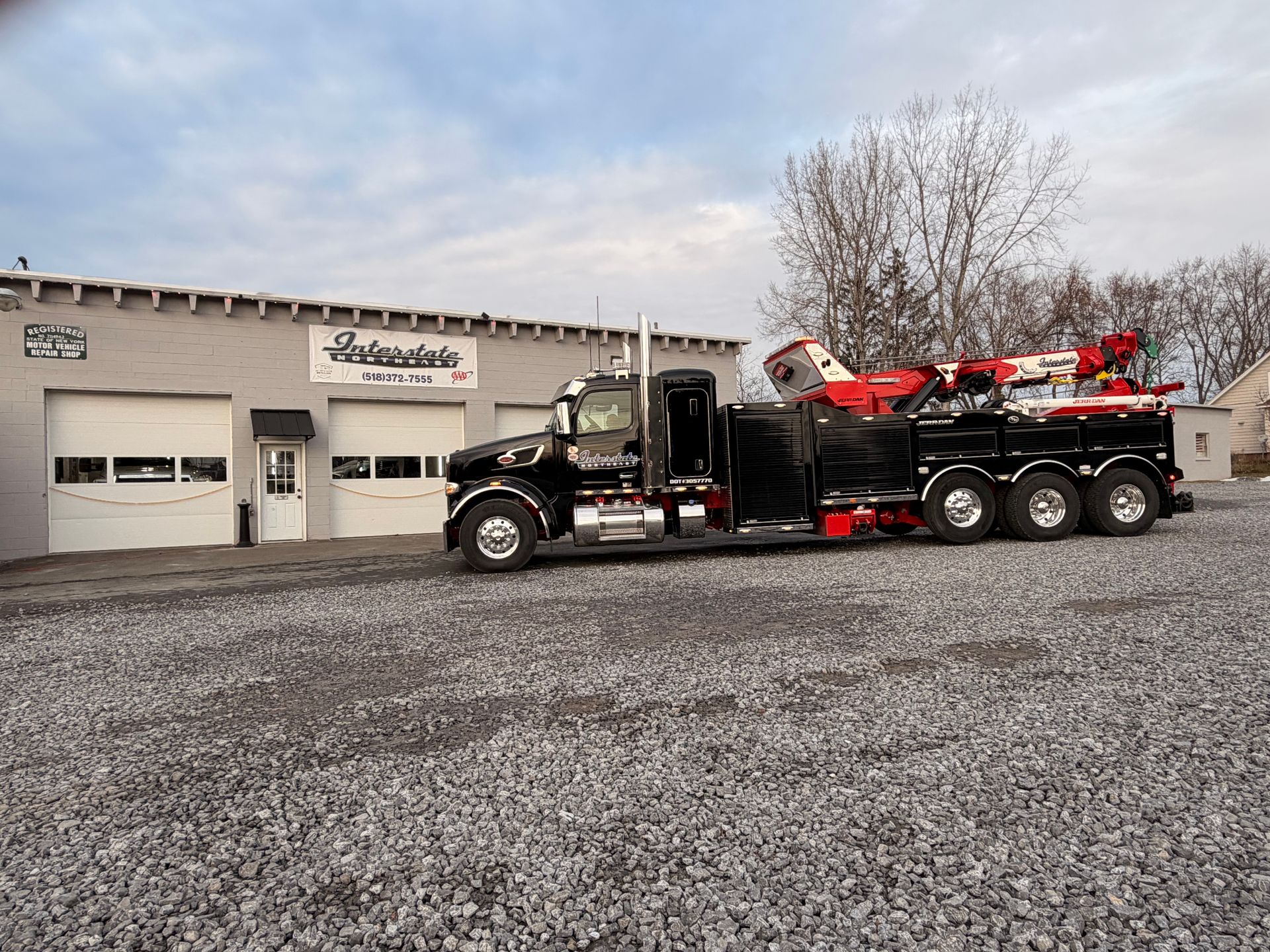 Black tow truck with red equipment parked outside a garage on a gravel lot.