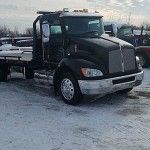 Black semi-truck parked in a snowy lot, front view with chrome bumper and grille.