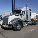 White semi-truck parked outdoors on a sunny lot, side view with silver fuel tanks and chrome bumper
