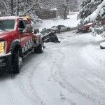 Snow-covered street with red pickup trucks and cars parked along a slushy, snowy road.