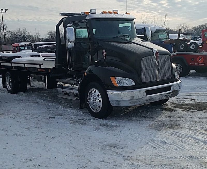 Black flatbed tow truck parked on snowy lot under overcast sky