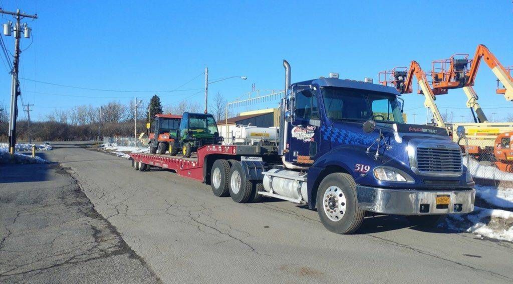 Blue semi truck hauling construction equipment on a road under a clear sky