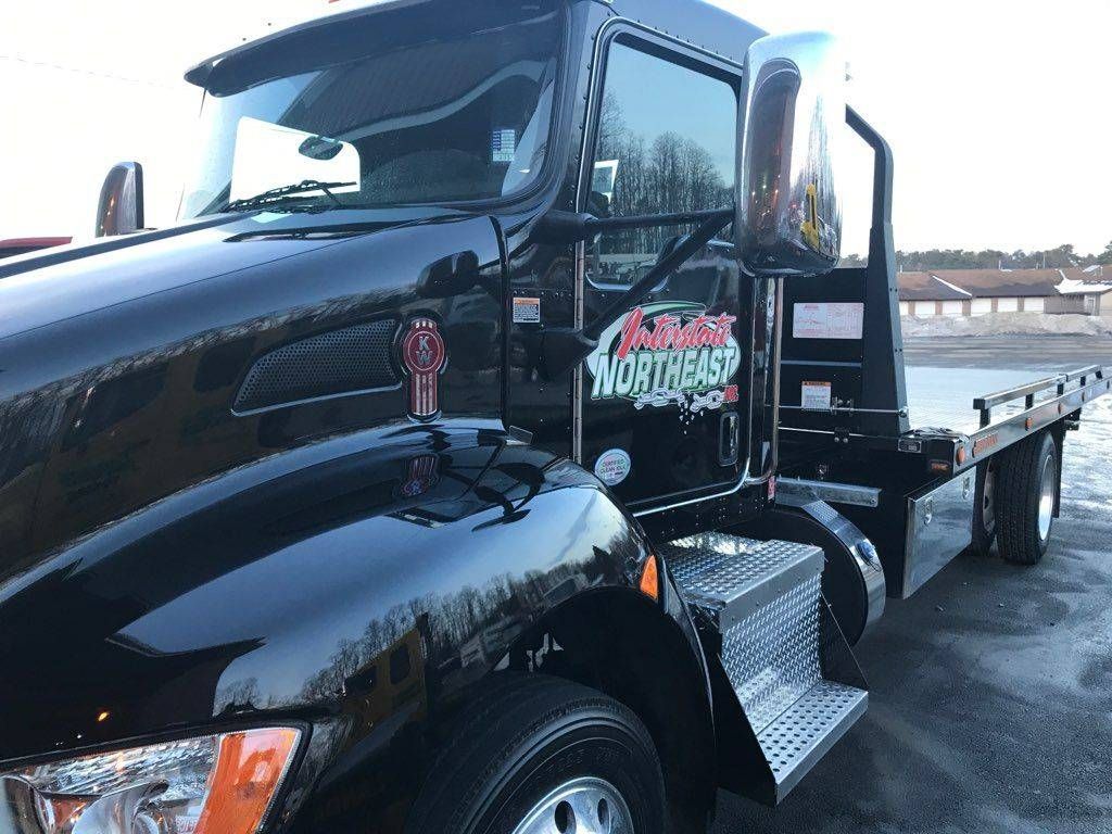 Black flatbed tow truck with chrome details parked outdoors near water