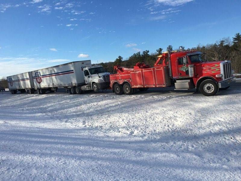 Red semi-truck hauling silver trailers on a snowy road under a blue sky.