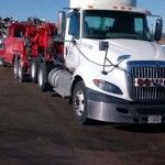 White semi truck towing a red car carrier trailer on a road