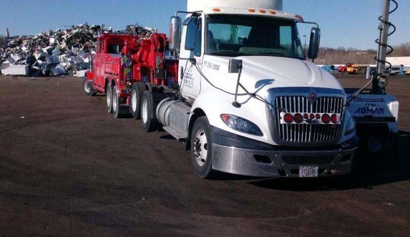 White semi truck hauling red wrecked cars in a salvage yard