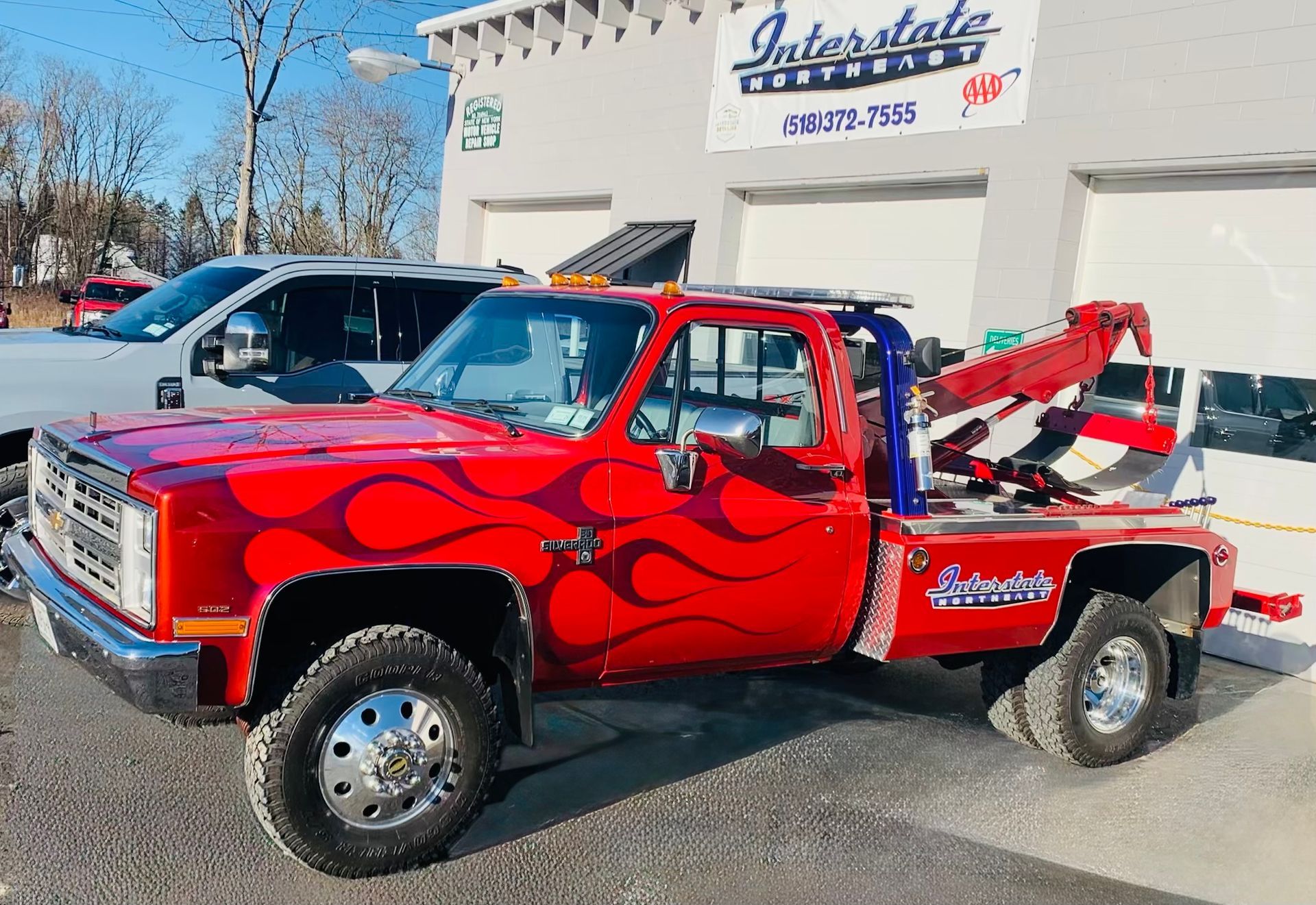 Red custom tow truck with flames parked outside a garage on a sunny day