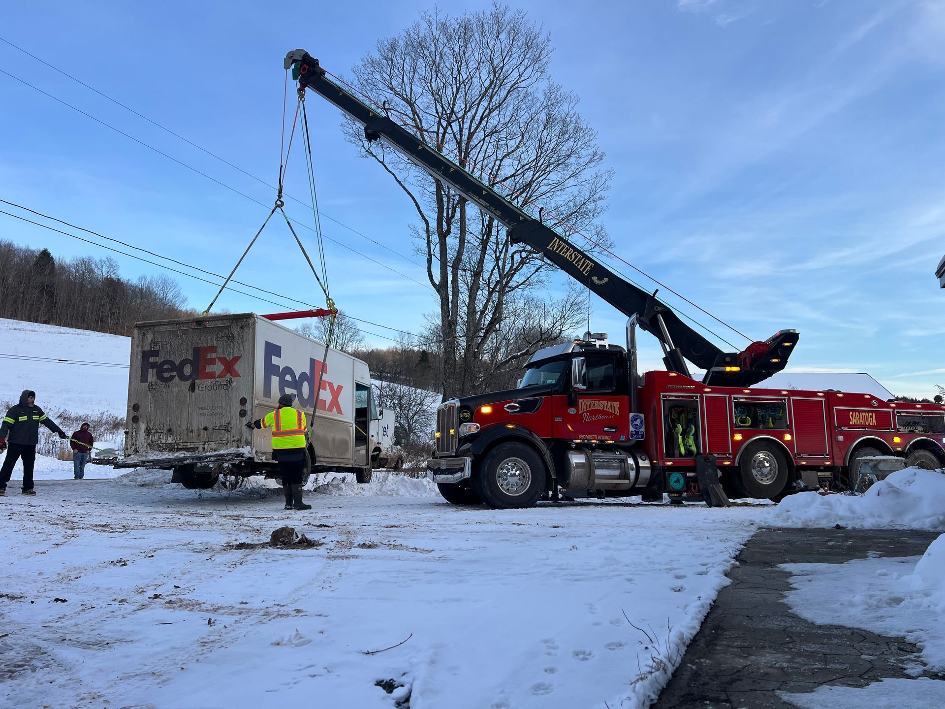 Tow truck lifting a FedEx trailer from a snowy roadside with workers nearby