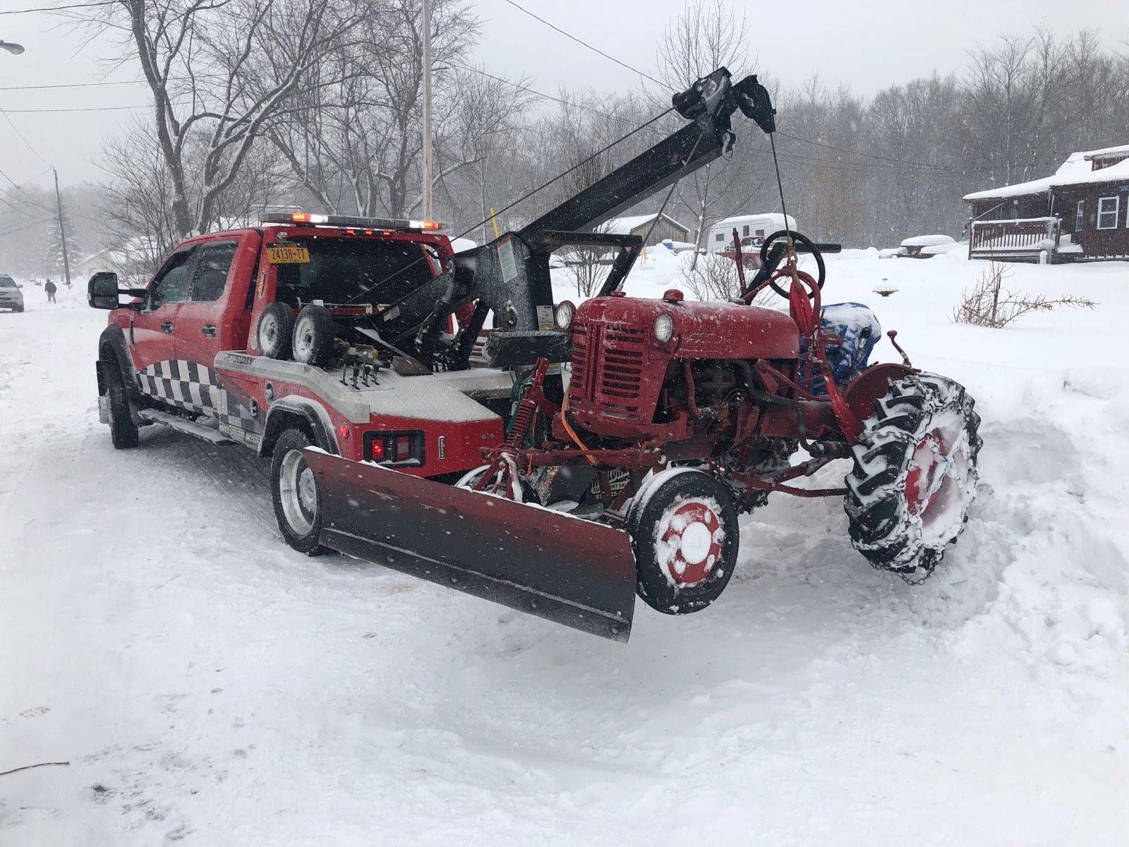 Red truck-mounted snow plow and tractor clearing snow on a snowy driveway