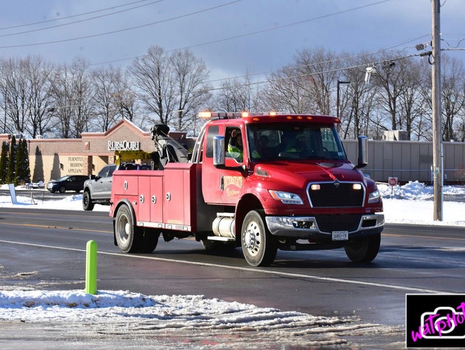 Red tow truck driving on a snowy street under a clear sky