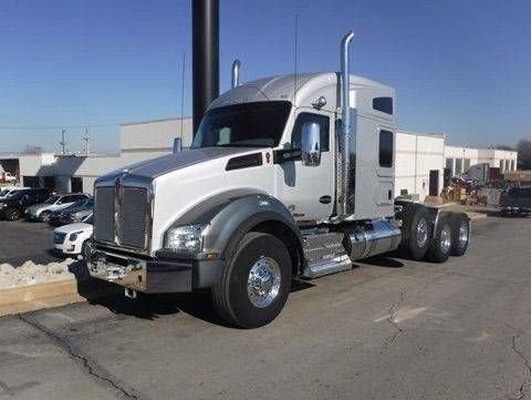 Silver semi-truck parked outdoors on a sunny lot, viewed from the front-left side.