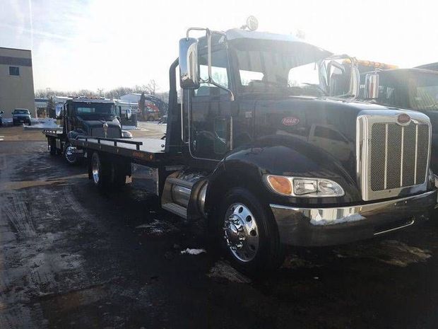 Black tow truck hauling a car on a flatbed in a wet parking lot