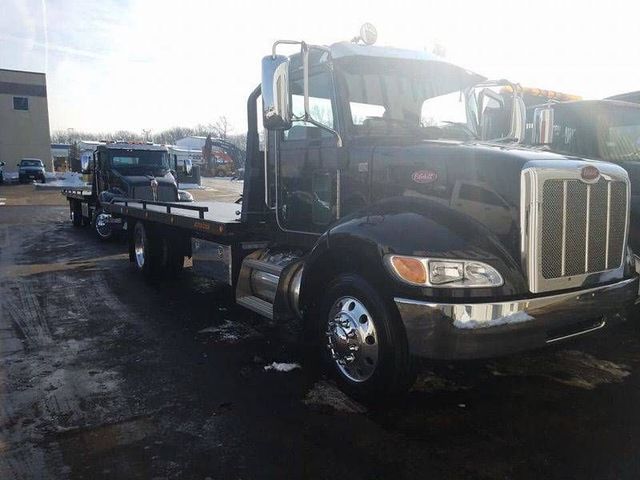 Black tow truck hauling a car on a flatbed in a wet parking lot