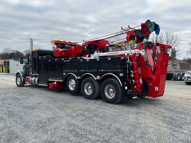 Red crane truck with black body parked on a gravel lot under an overcast sky.
