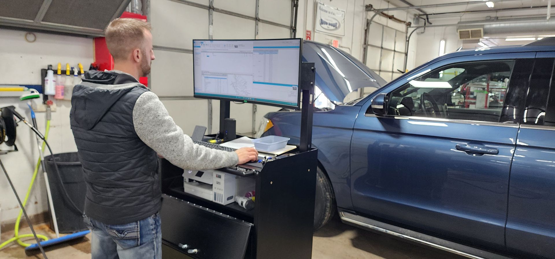 A man is working on a computer in a garage next to a car.