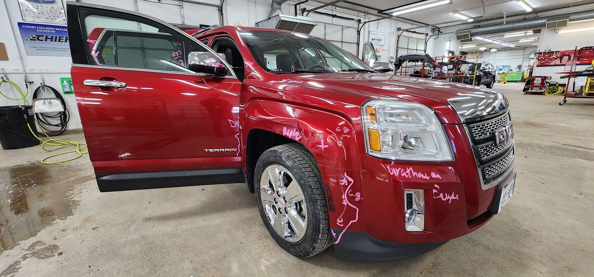 A red gmc terrain is parked in a garage with its doors open.