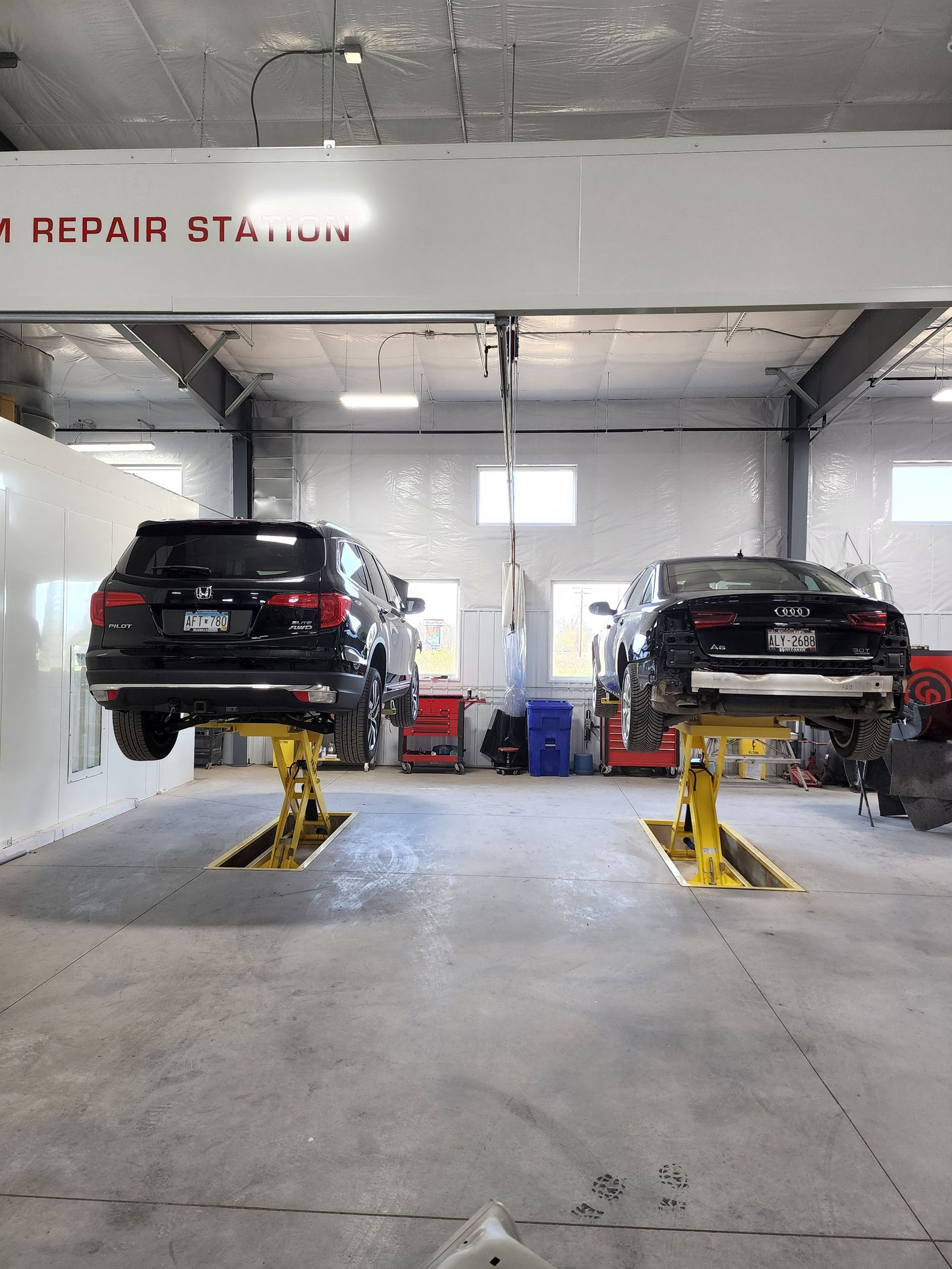 Two cars are sitting on a lift in a garage.
