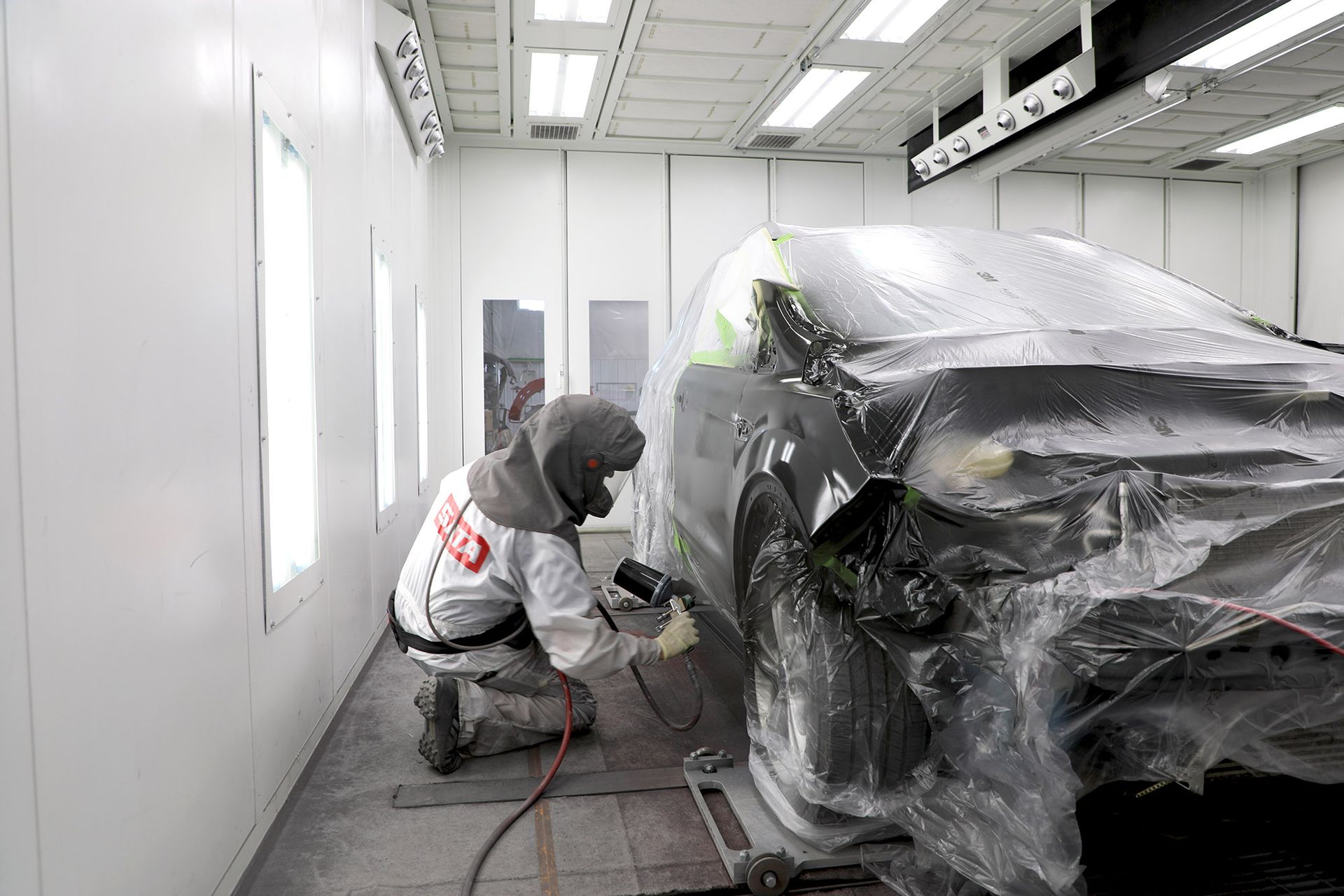 A man is painting a car in a paint booth.