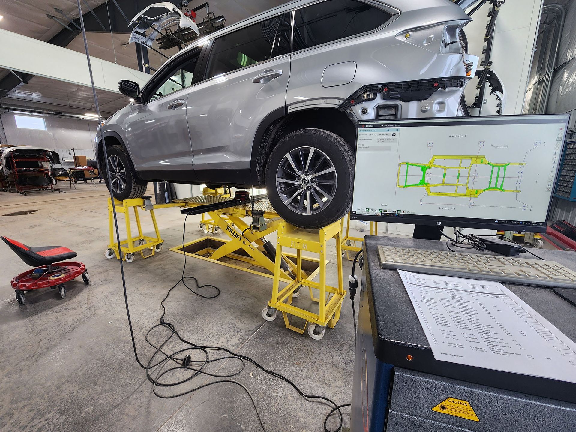 A car is sitting on a lift in a garage next to a computer monitor.