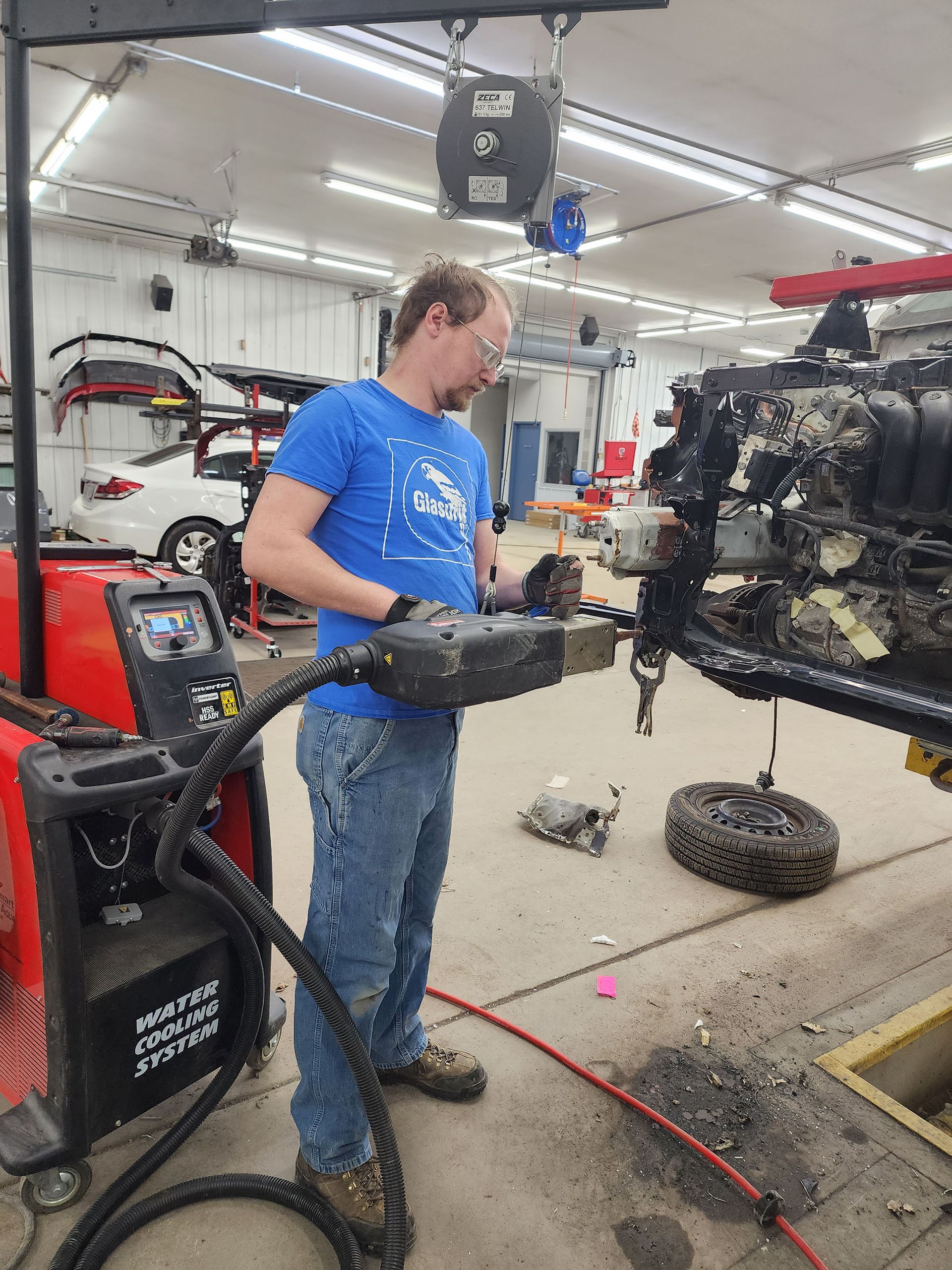 A man in a blue shirt is working on a machine in a garage.