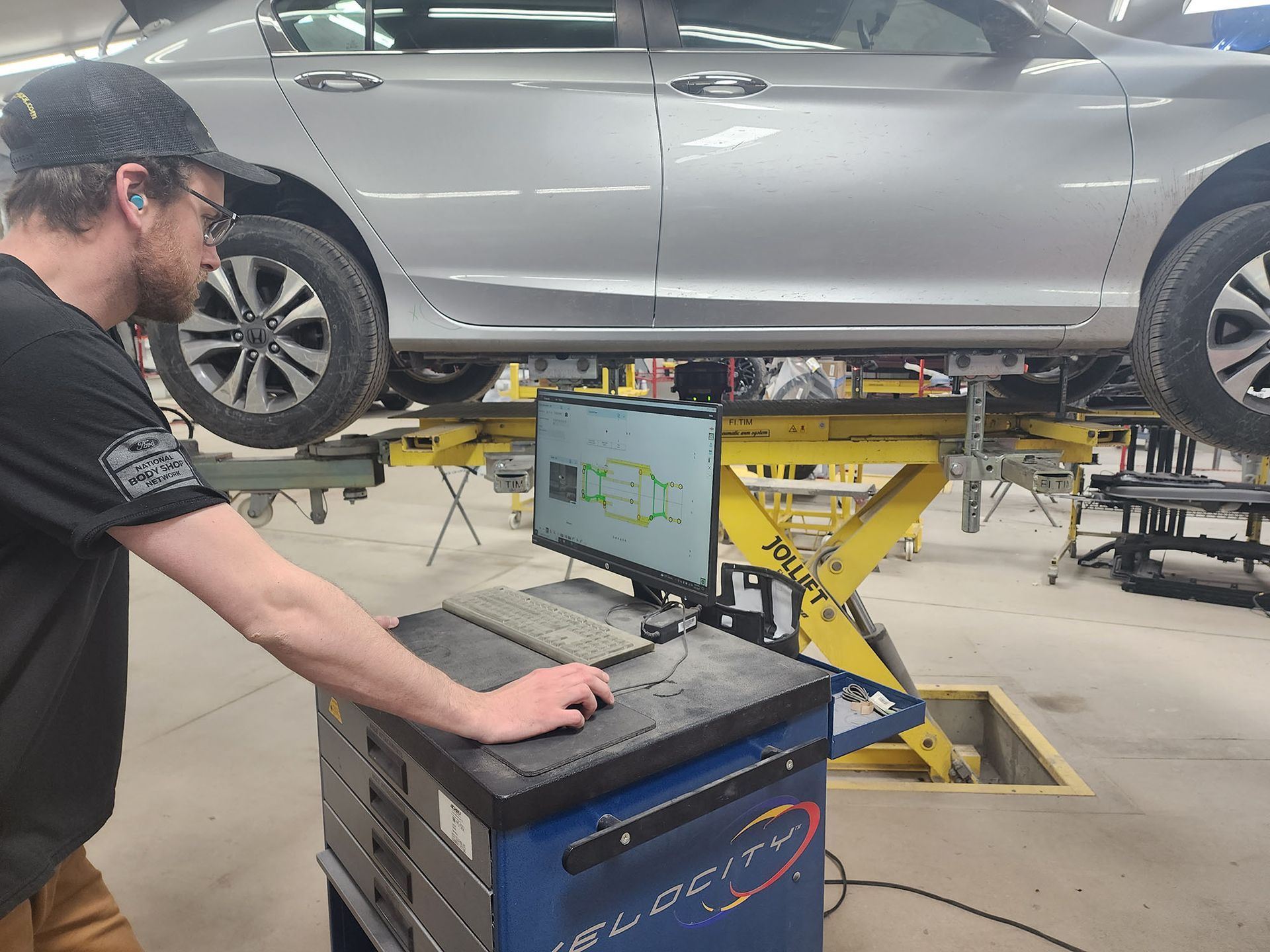 A man is working on a computer in front of a car on a lift.