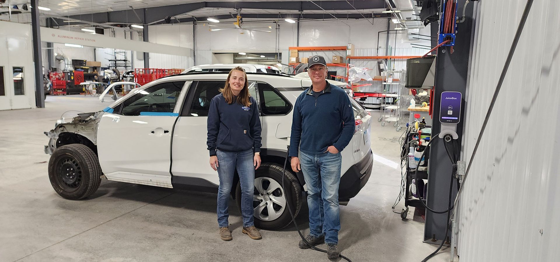 A man and a woman are standing next to a white suv in a garage.